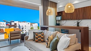 A modern living room with a sofa, a coffee table, and a dining area. There is a view of buildings outside the window. - 1 BR Golden Zone · Luxury Beach and Infinity Pool (Bucerías)