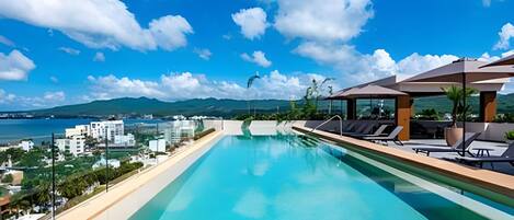 A rooftop infinity pool with a clear view of the sea and mountains.