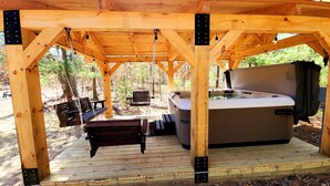 Een houten terras met een hottub, banken en een schommel.