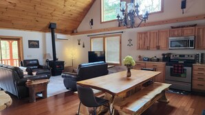Een gezellige woonkamer met een open haard, leren banken, een houten eettafel en een keuken met moderne apparatuur.