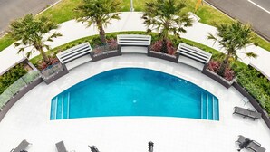 Une piscine aux bords incurvés, dotée d’une terrasse carrelée de blanc, entourée de palmiers et d’une rambarde blanche.
