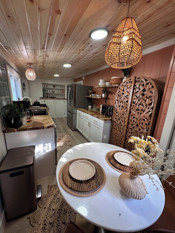 A modern kitchen with wooden cabinets, a stainless steel refrigerator, and a dining area with a round table and placemats.