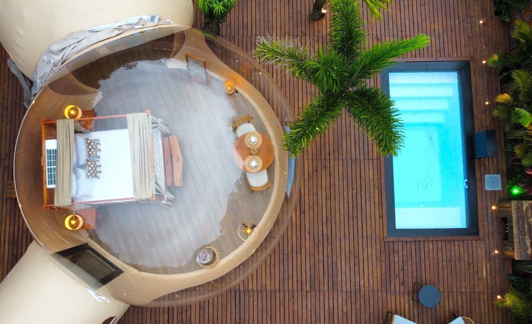 A circular hot tub with a bed and seating area, surrounded by wooden decking and potted plants.