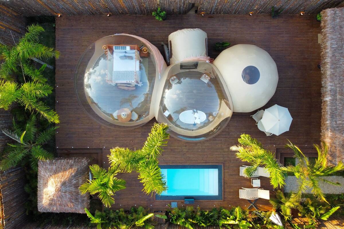 An aerial view of a rooftop with a swimming pool, two hot tubs, and a seating area with umbrellas.