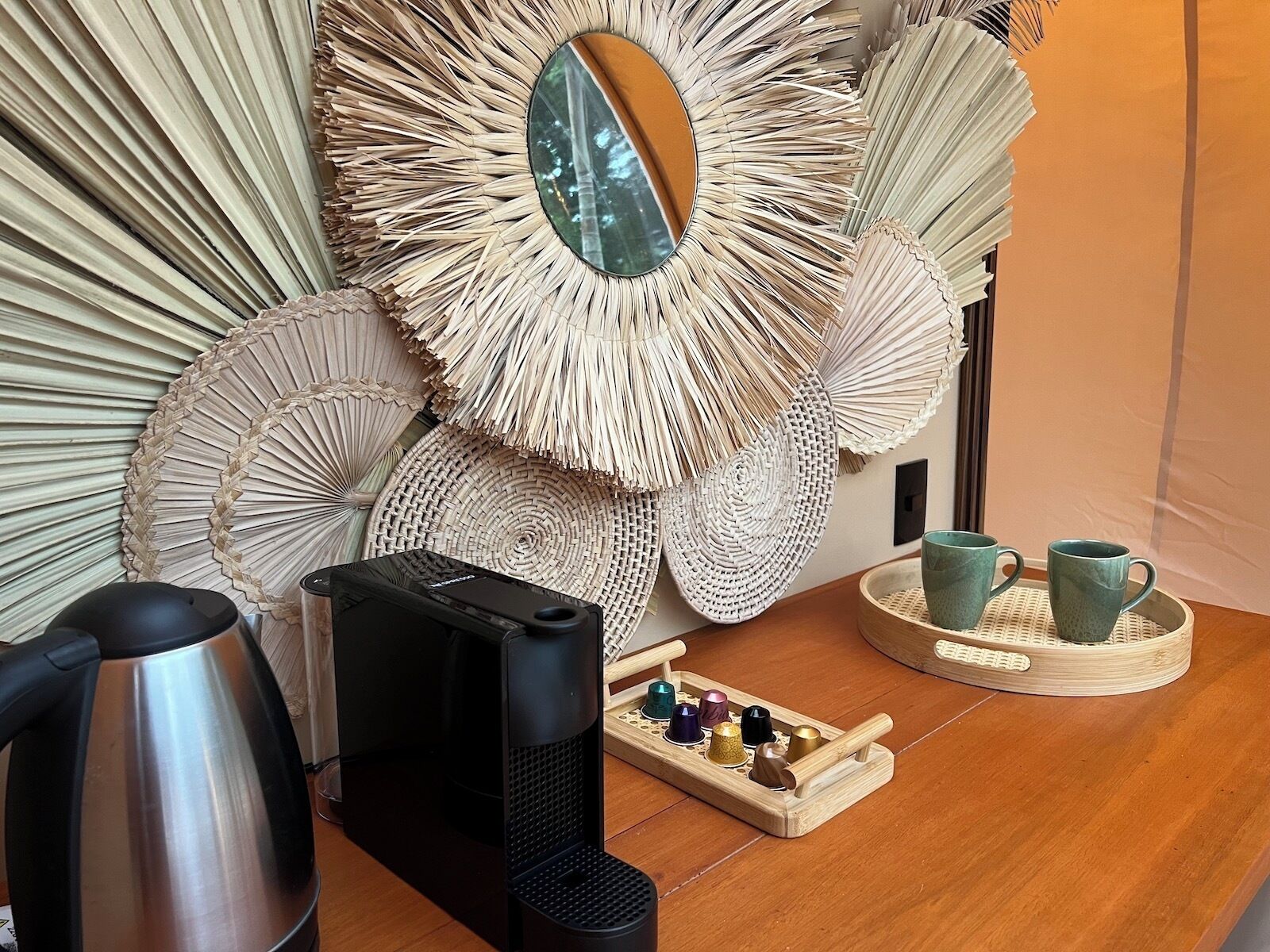 A room with a large woven wall art piece, a coffee maker, a kettle, and a tray with colorful cups.