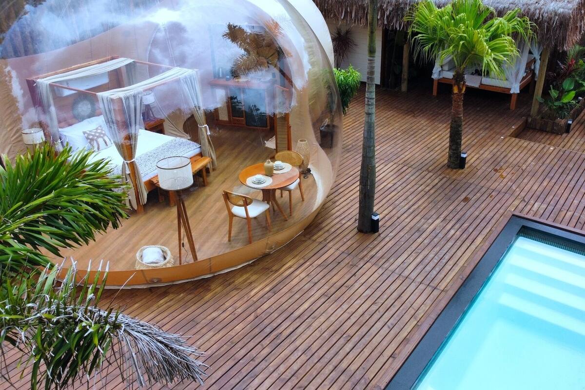 A transparent dome structure with a dining area, a hot tub, and a pool.