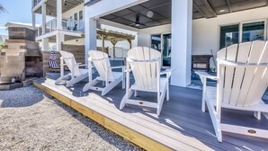 Eine Terrasse mit weißen Adirondack-Stühlen, einem Grill und einer Pergola.