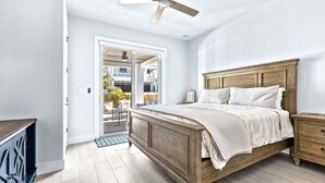 Ein Schlafzimmer mit einem hölzernen Bett, einem Deckenventilator und Blick durch eine geöffnete Tür auf einen Außenbereich.