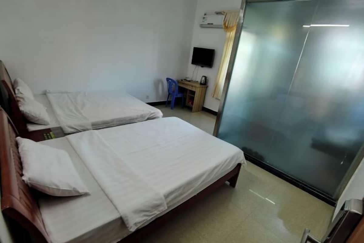 A hotel room with two beds, a desk with a chair, a television, and a sliding glass door.