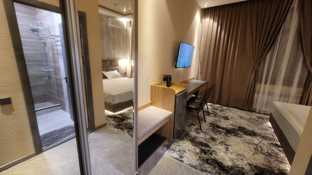 Una camera d'albergo con un letto, una scrivania con una sedia, una televisione e un box doccia.