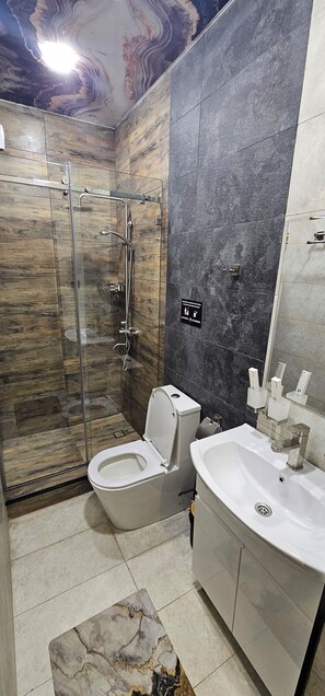 A modern bathroom with a glass-enclosed shower, a white toilet, and a large sink with a mirror. - Homy House Hotel (Tashkent)
