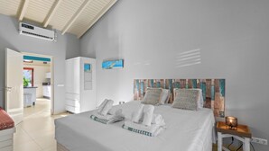 Une chambre d’hôtel avec un lit, une table de chevet avec une lampe, une armoire et une salle de bain visible à travers une porte ouverte.