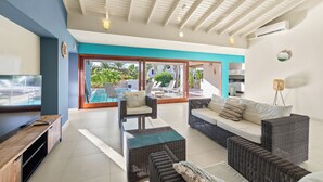 Un salon moderne avec des meubles en osier, un téléviseur et une vue sur la piscine.