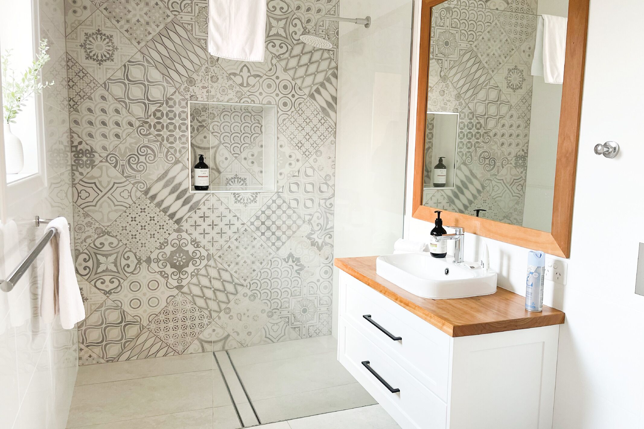Un baño con baldosas estampadas, un lavabo con encimera de madera, un espejo y un perchero para toallas.