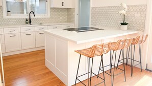 Una cocina moderna con armarios blancos, una isla grande con taburetes y un salpicadero de baldosas hexagonales.
