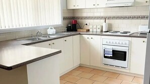 A kitchen with white cabinets, a built-in oven, a coffee maker, and a window with blinds.