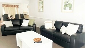 A modern living room with two black leather sofas, a white coffee table, and framed artwork on the walls.
