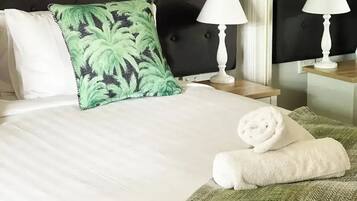 A neatly made bed with white linens, a green patterned pillow, and a rolled white towel on a green herringbone throw.
