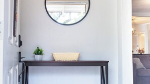 Een gang met een donkere console tafel, een ronde spiegel en een potplant.