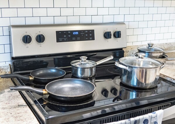 Une cuisine équipée d’une cuisinière en acier inoxydable, de quatre casseroles et de poêles posées sur la plaque de cuisson.