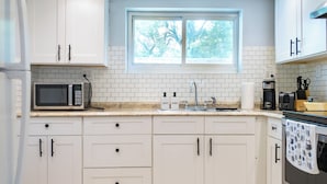 Een moderne keuken met witte kastjes, een magnetron, een spoelbak en een raam met uitzicht op bomen.