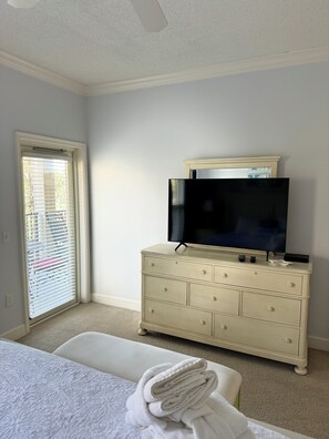 Un dormitorio con cama, cómoda, televisor y ventana con persianas.