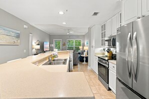 A modern kitchen with stainless steel appliances, a central island, and a view of the beach through the windows.