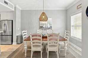 A modern kitchen with a dining table, chairs, a refrigerator, and a hanging light fixture.