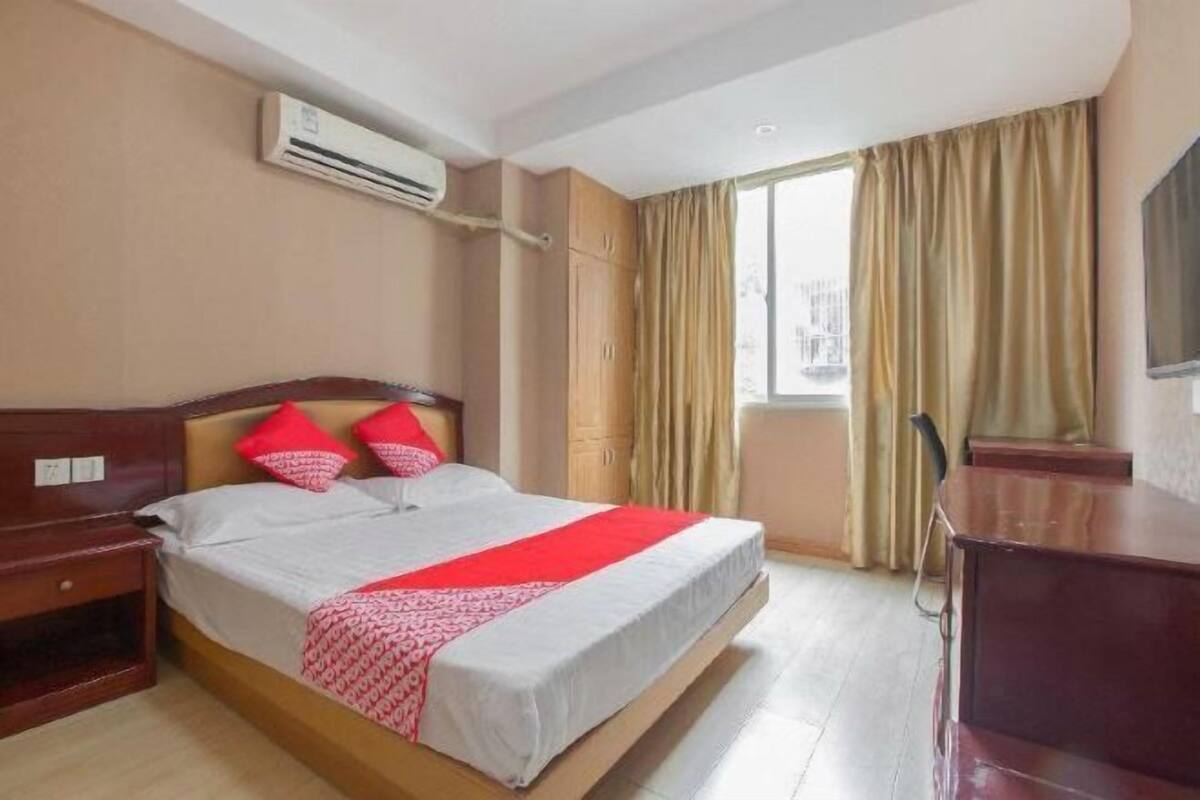 Una habitación de hotel con cama, escritorio, aire acondicionado y ventana con cortinas.