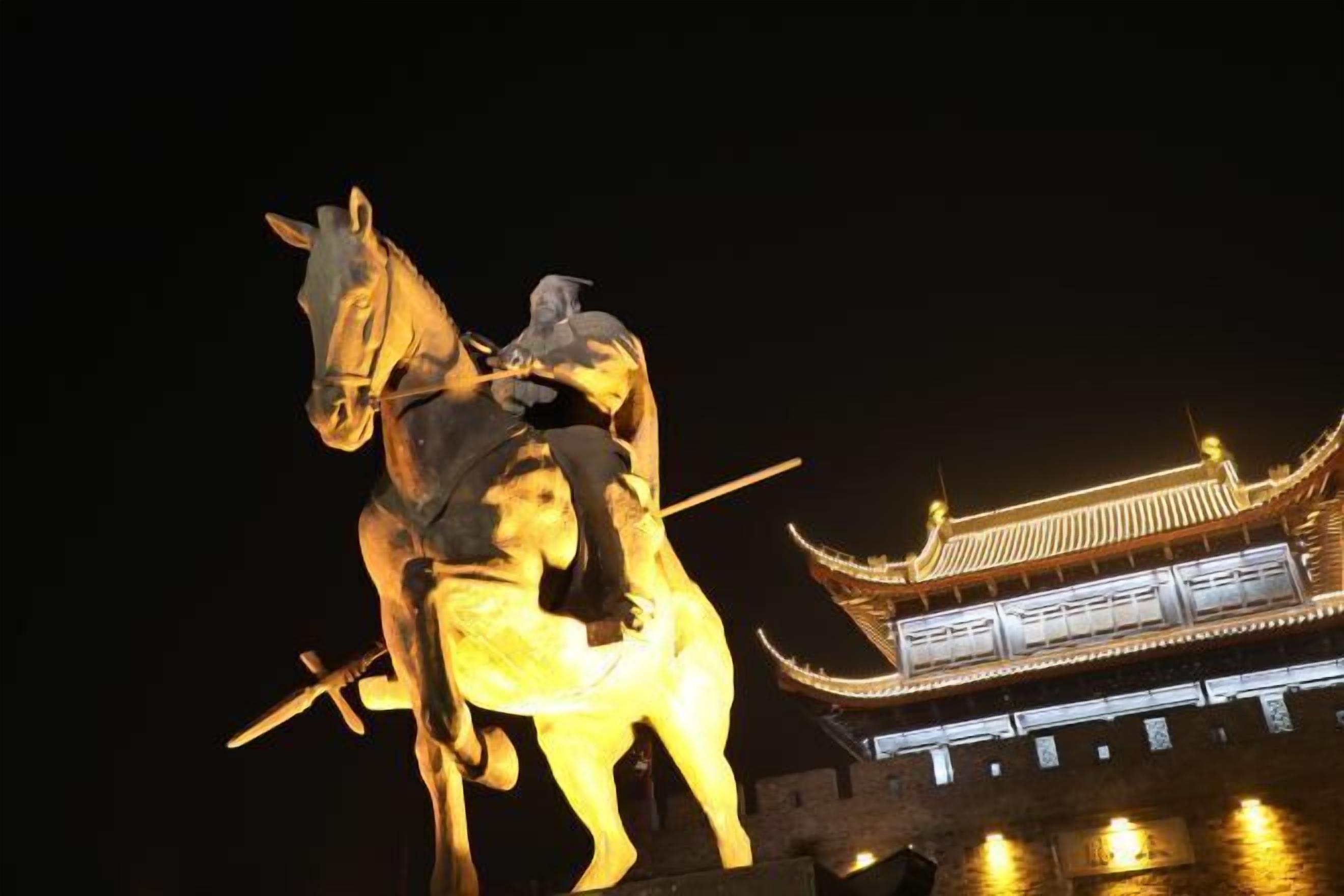 A statue of a figure on horseback with a sword, set against a traditional building with illuminated windows.