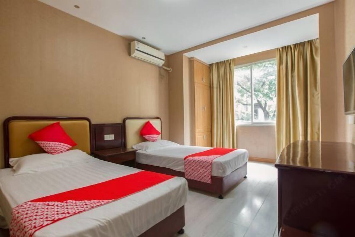 Habitación de hotel con dos camas, un escritorio y un ventanal grande con cortinas.