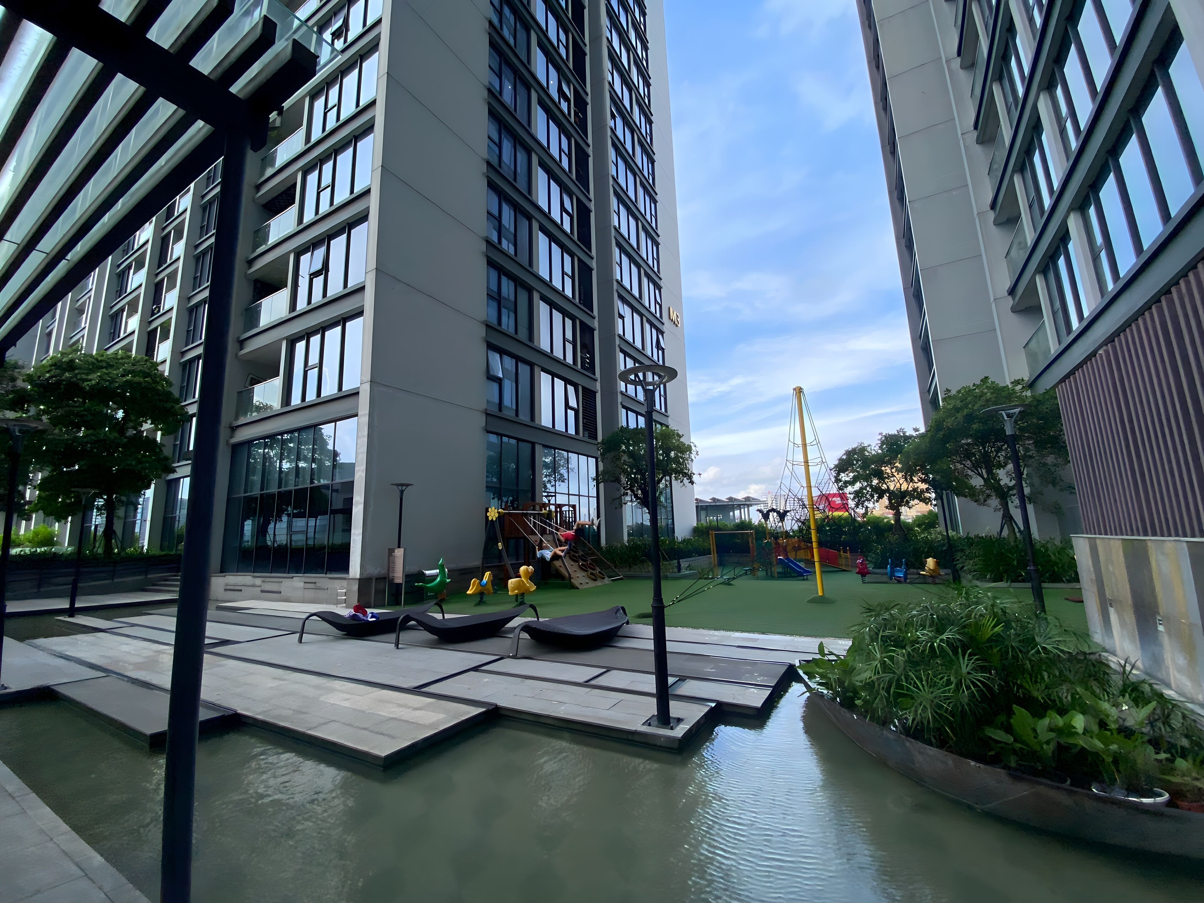 A modern building with a water feature in front, surrounded by greenery and a playground.