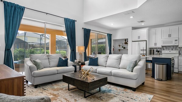A modern living room with two sofas, a coffee table, and a view of a kitchen and outdoor area.