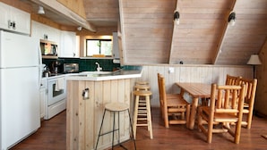 A kitchen with wooden cabinets, a central island, stools, and a dining table with chairs. - Smoky Mtn Escape | Indoor Pool, Arcade, Theater & Firepit Nights (Gatlinburg)