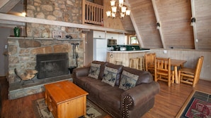 A cozy loft-style living area with a stone fireplace, wooden furniture, and a high ceiling with exposed beams. - Smoky Mtn Escape | Indoor Pool, Arcade, Theater & Firepit Nights (Gatlinburg)
