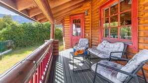 A wooden cabin with a porch, two chairs, a table, and a view of a mountain. - Serene 2-bedroom house with WiFi in Arucas (arucas)