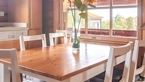 A wooden dining table with white chairs, a vase with sunflowers, and a window with a view of greenery and buildings. - Serene 2-bedroom house with WiFi in Arucas (arucas)
