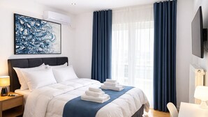 Habitación de hotel con cama, mesita de noche, escritorio, silla, televisor y ventana con cortinas.