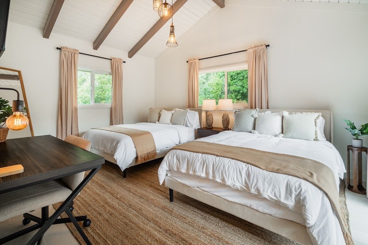 Une chambre avec deux lits, un bureau en bois et une grande fenêtre avec des rideaux.