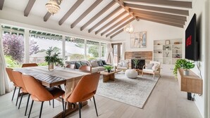 A modern living room with a dining area, large windows, and a fireplace.