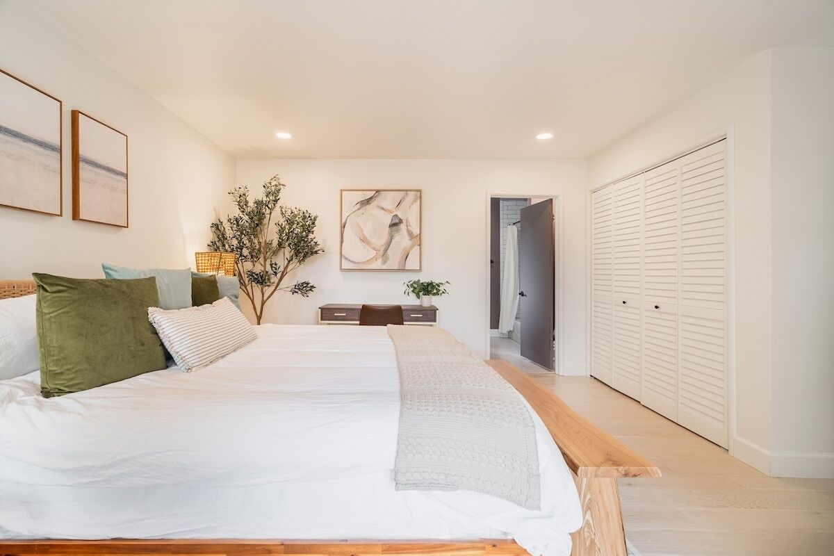 A bedroom with a large bed, a bedside table, a mirror, and a wardrobe.