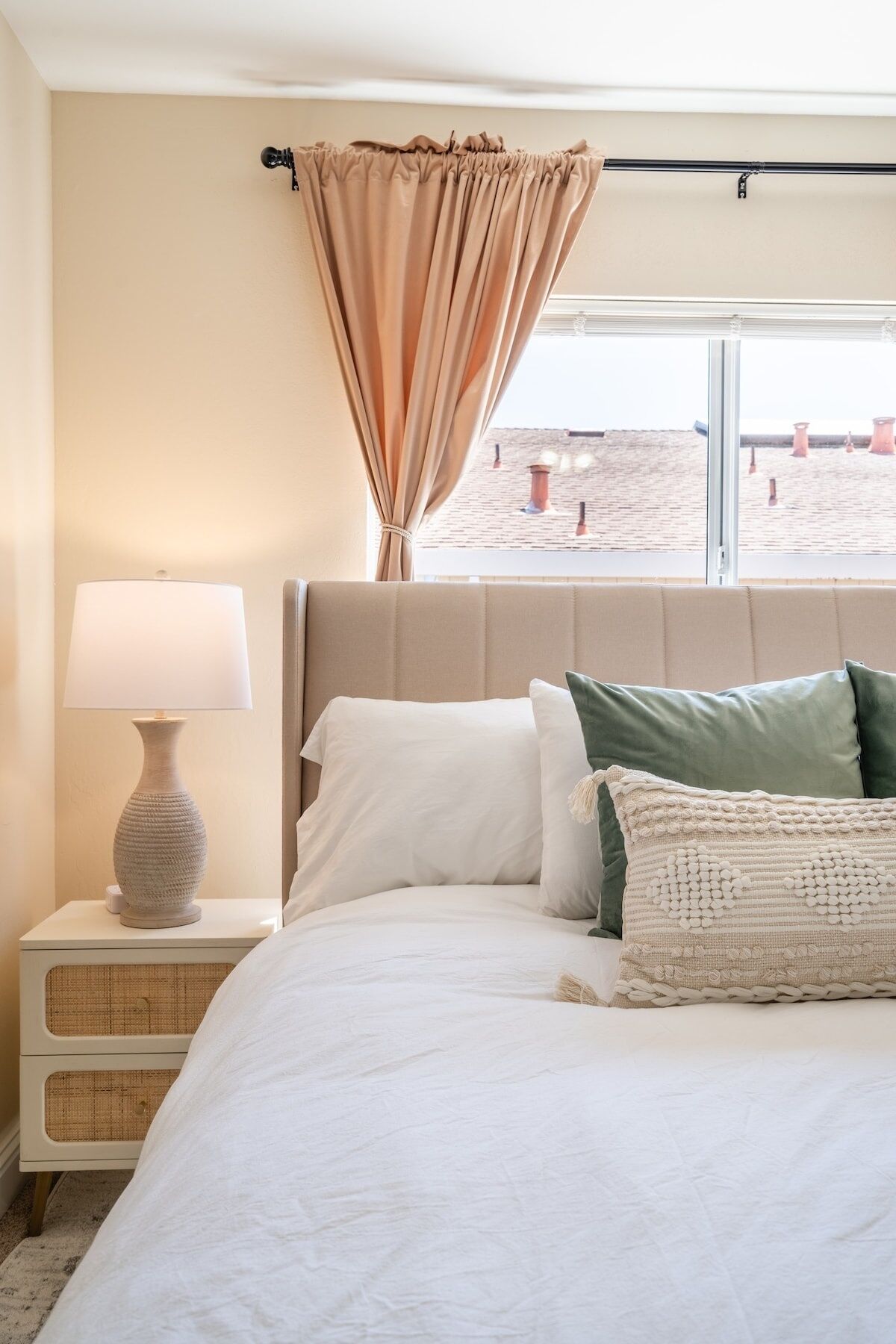 Un dormitorio con cama, mesita de noche, lámpara y vistas al exterior.