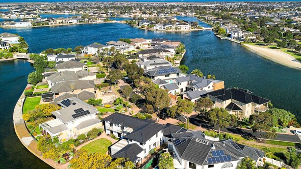 Área residencial com casas ao longo de uma orla curva, com painéis solares nos telhados e vista clara da água.