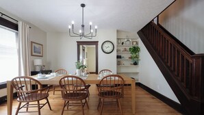 Uma sala de jantar com mesa e cadeiras de madeira, um lustre, um relógio e uma escadaria.
