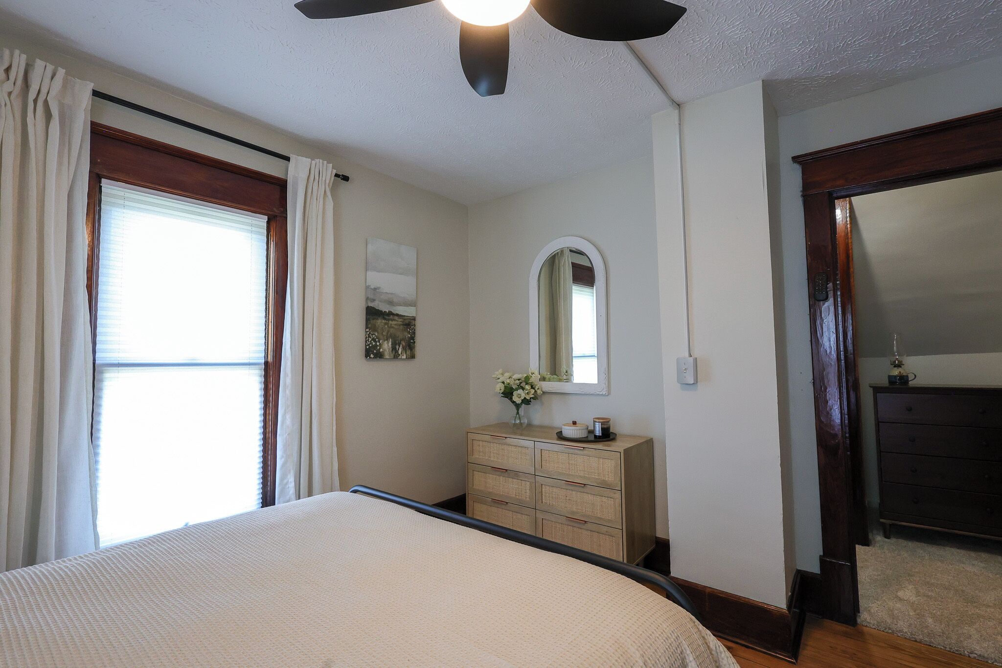 A bedroom with a bed, a dresser, a mirror, and a ceiling fan.