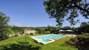 A swimming pool with lounge chairs, a stone building, and a grassy area with trees. - Mulino della Villa (Bucine)