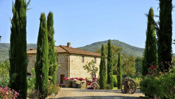 A stone building with a tiled roof, surrounded by tall cypress trees and a gravel path leading to a wooden cart. - Mulino della Villa (Bucine)