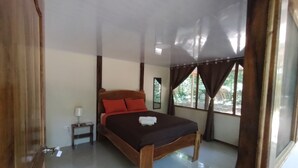 A bedroom with a wooden bed, a nightstand, and a window with curtains. - Cool Waters Jungle Camping (Bahía Ballena)