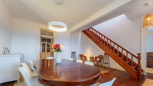 A dining area with a wooden table, white chairs, a vase with flowers, a staircase, and a white wall. - FLH Funchal Casa do Carvalhal (Funchal)