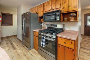 A compact kitchen with wooden cabinets, a stainless steel refrigerator, a microwave, a gas stove, and an oven.